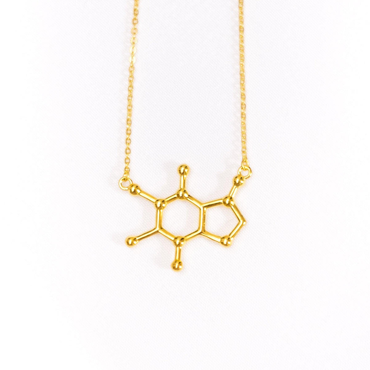 Gold necklace with a molecular design pendant on a white background