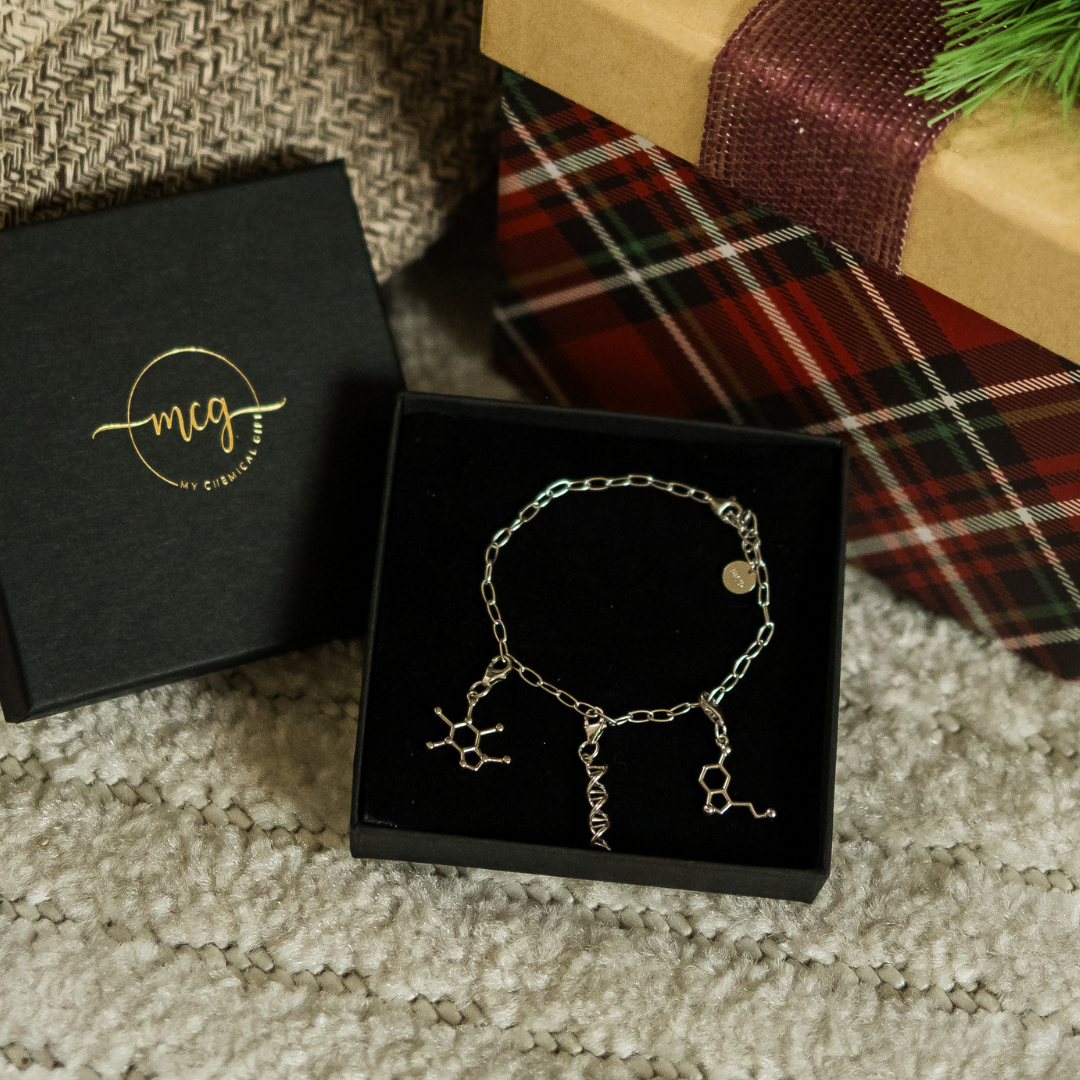 Bracelet with molecular designs in a black box, next to a branded box and plaid fabric.
