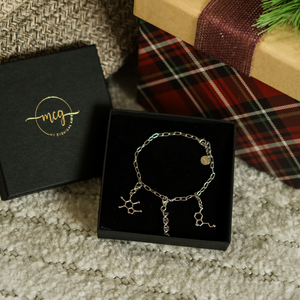 Bracelet with molecular designs in a black box, next to a branded box and plaid fabric.