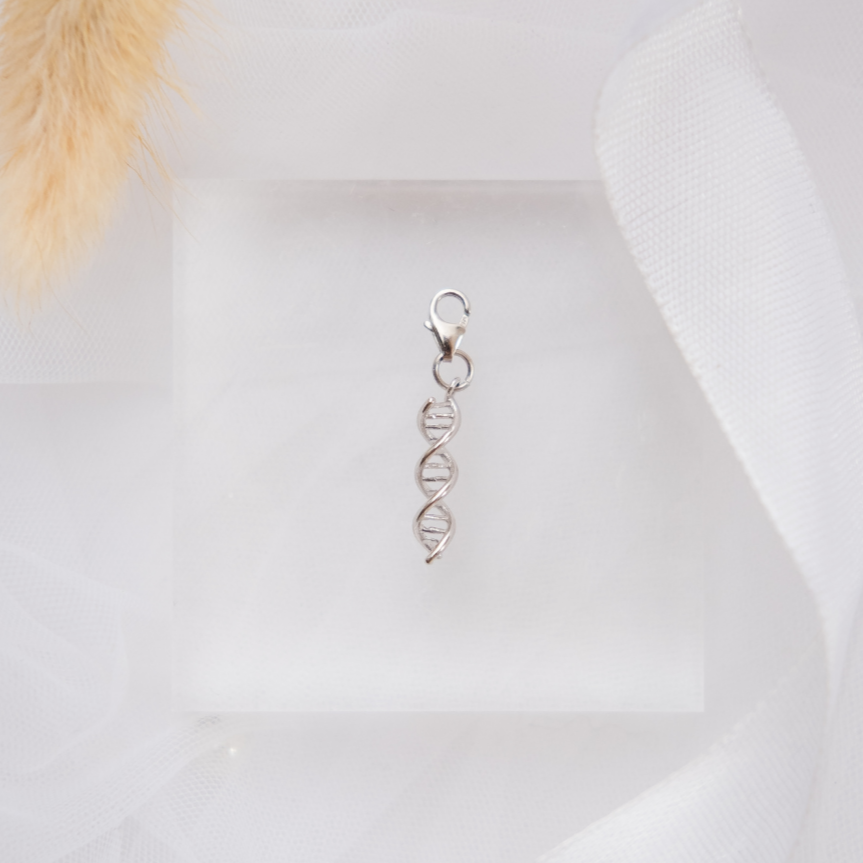 Silver DNA-shaped pendant on a white fabric background with decorative elements.