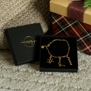Gold bracelet with molecular designs in a black box on a textured surface.