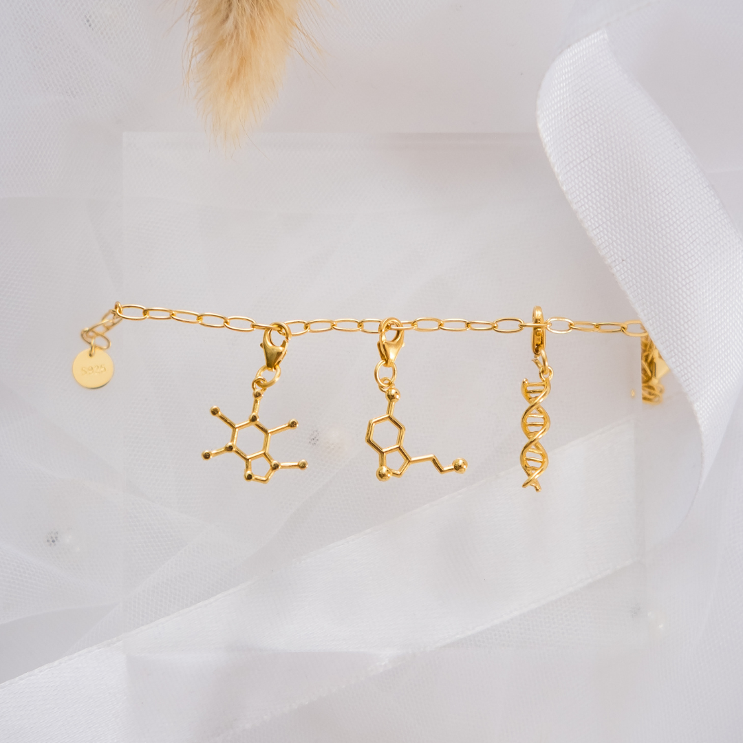 Gold bracelet with molecular design charms on a white fabric background