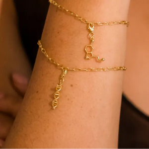 Model wearing DNA double helix and serotonin molecule gold charm bracelet - chemistry inspired jewellery for science lovers 