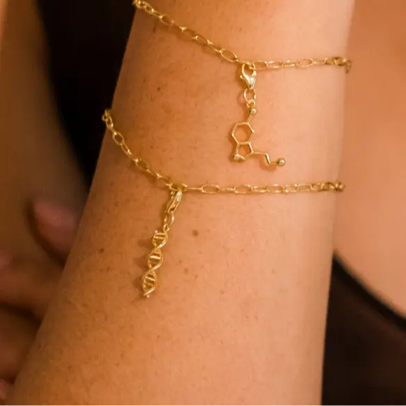 Model wearing DNA double helix and serotonin molecule gold charm bracelet - chemistry inspired jewellery for science lovers 