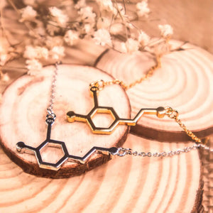 Dopamine molecule necklace in gold and in silver on a wooden background - chemistry inspired jewellery for science lovers 