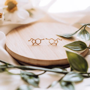 Serotonin molecule earrings in gold on a wooden background - chemistry inspired jewellery for science lovers 